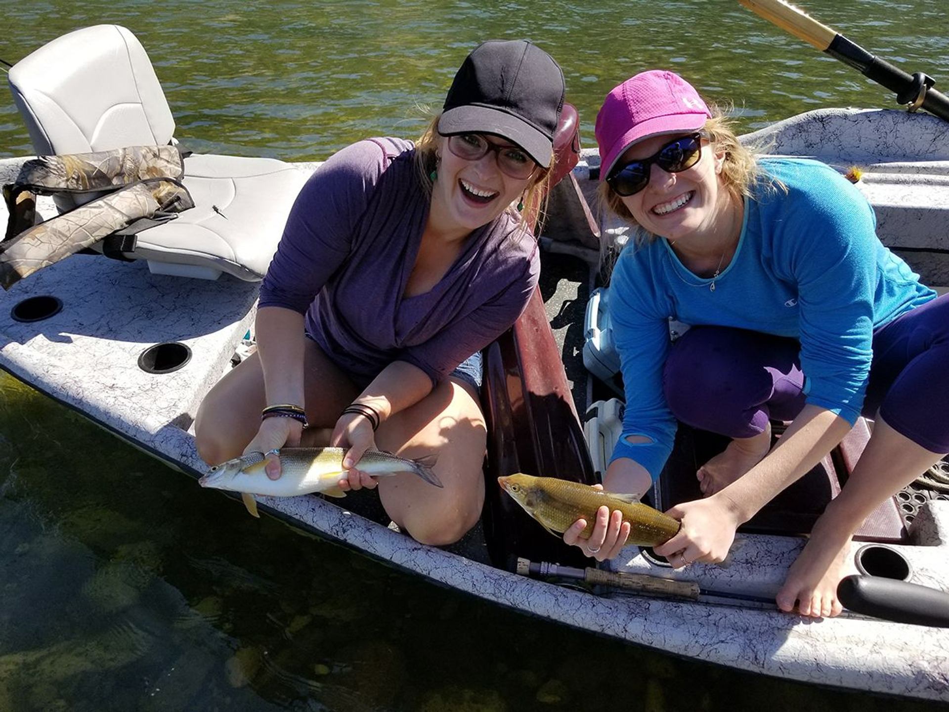 Two women kneel in a boat, each holding a fish.