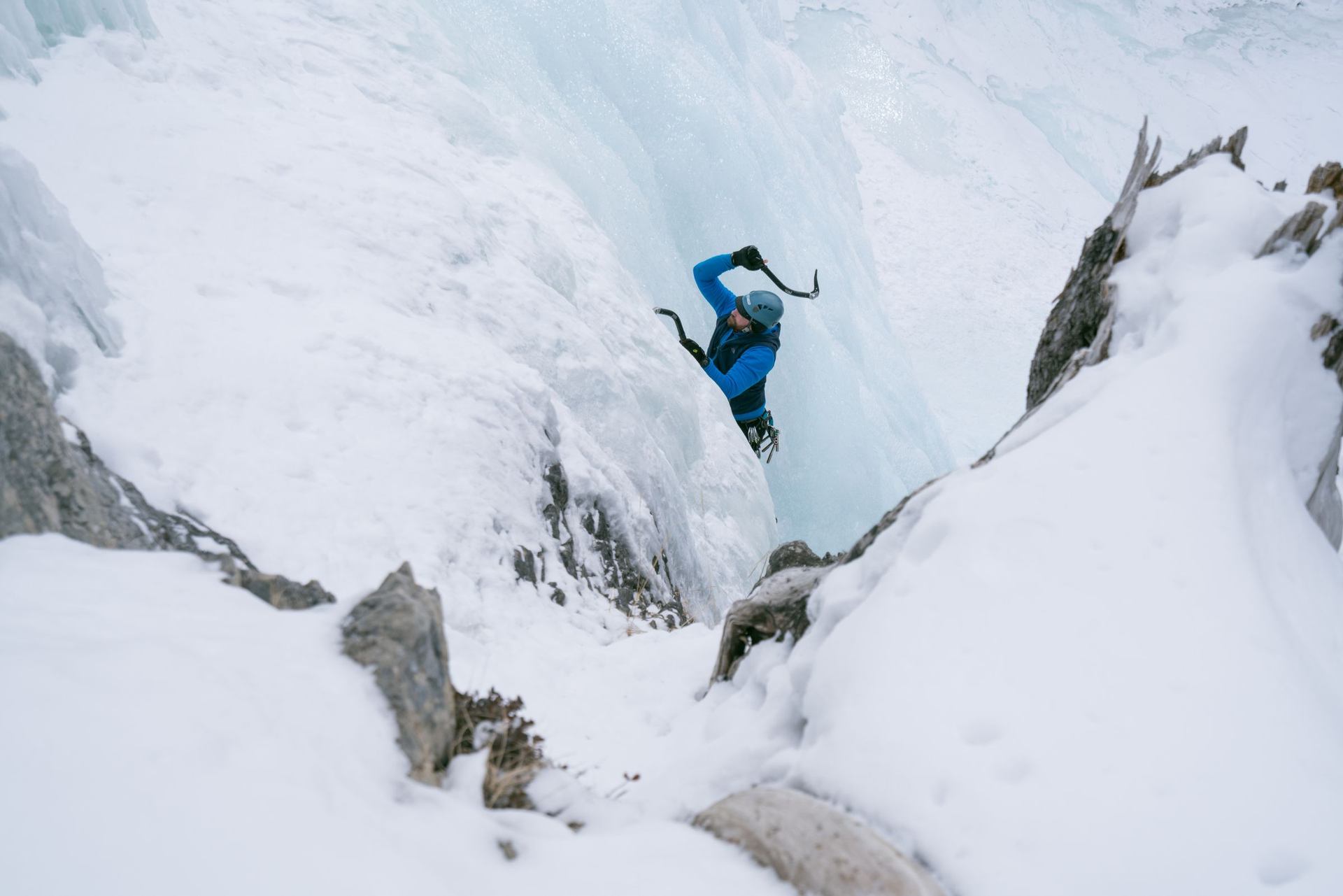 An ice climber surrounded by snow and ice, uses his ice pick at Tangle Falls in Jasper National Park