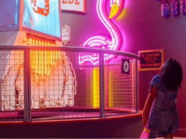 A child looks up in a room filled with neon lights and sculptures.