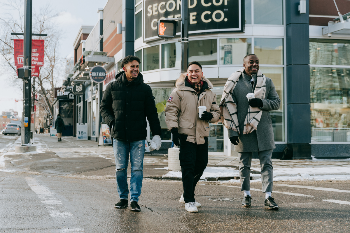 The men traverse a crosswalk holding coffee cups.