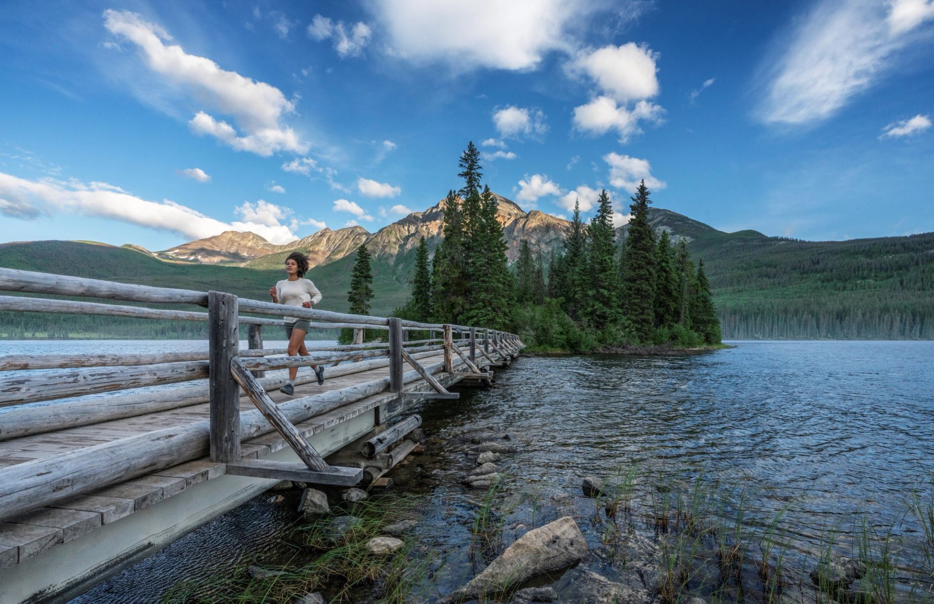 A women running across a bridge surrounded by water at Pyramid Lake in Jasper National Park.