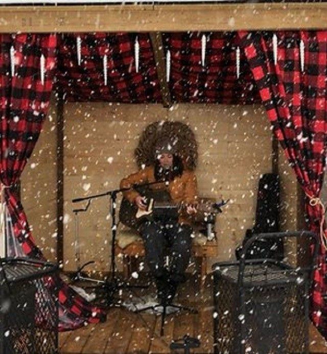 A guitarist plays on a small stage while snow falls.
