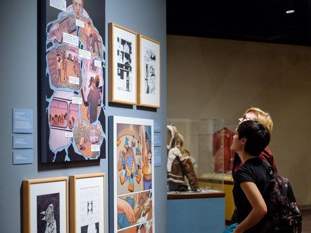 Two people look upon a wall covered in different artwork.