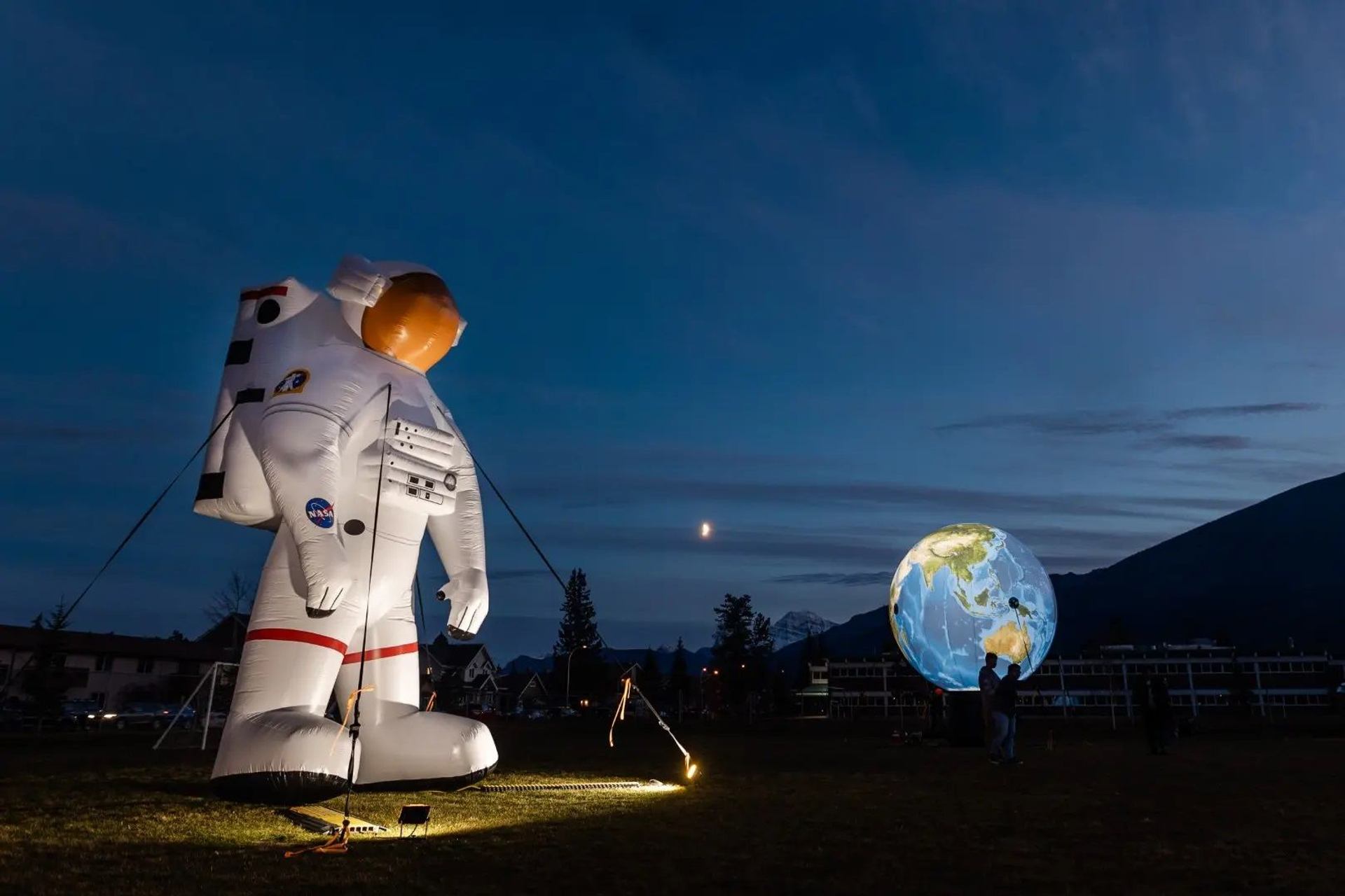 A giant inflatable astronaut and translucent globe are illuminated at night.