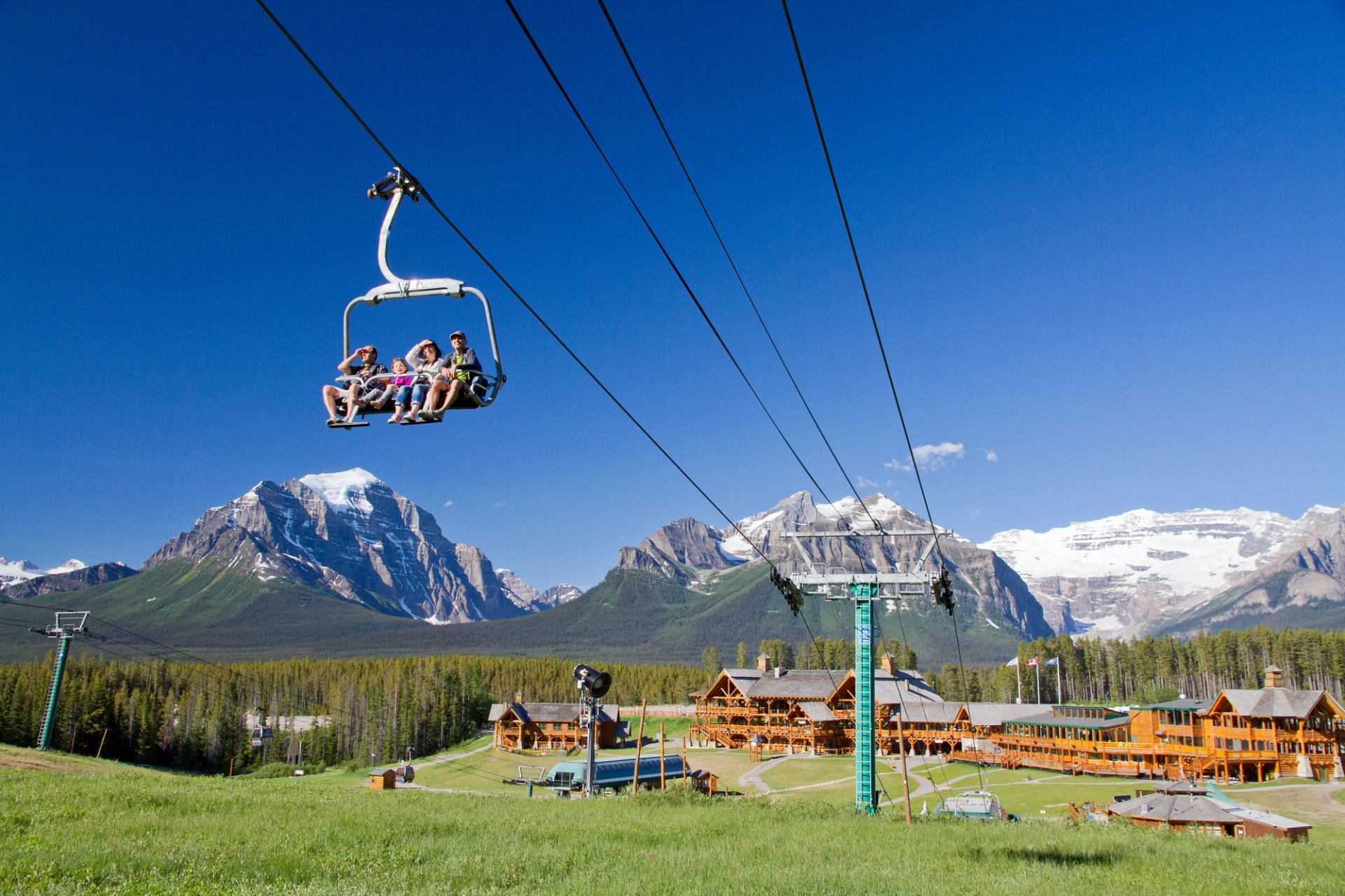 People riding a chairlift in the summer with views of the lodge building at Lake Louise in Banff National Park.