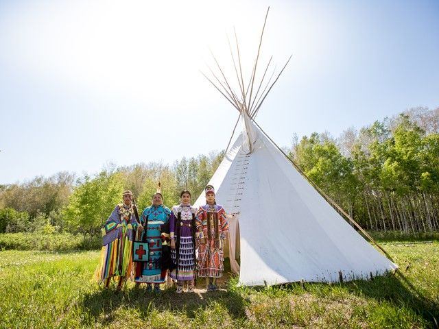 Siksika Blackfoot dancers standing in front of a tipi in Tipi Village.