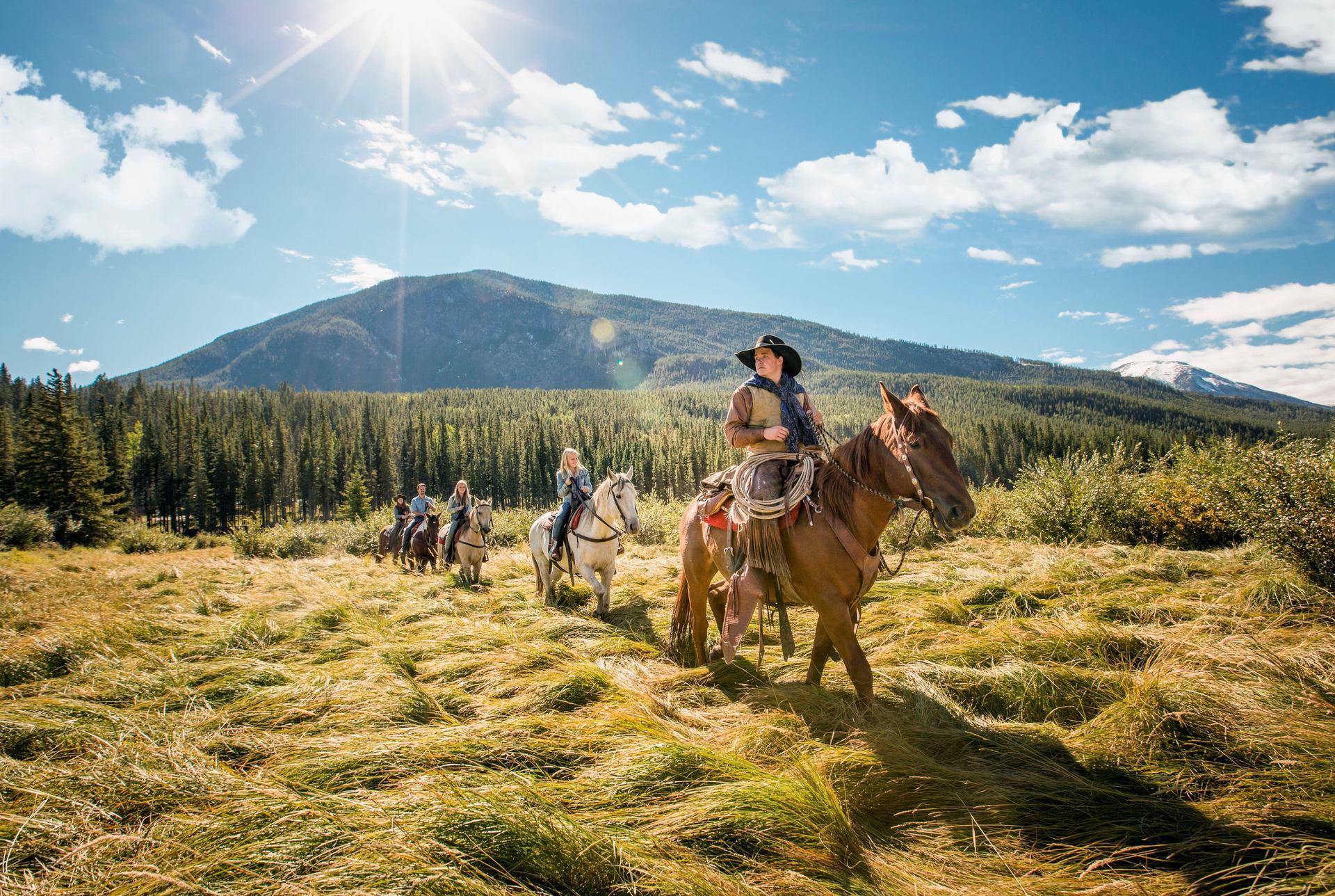 People on a trail riding through a grassy field in the mountains in Banff National Park.