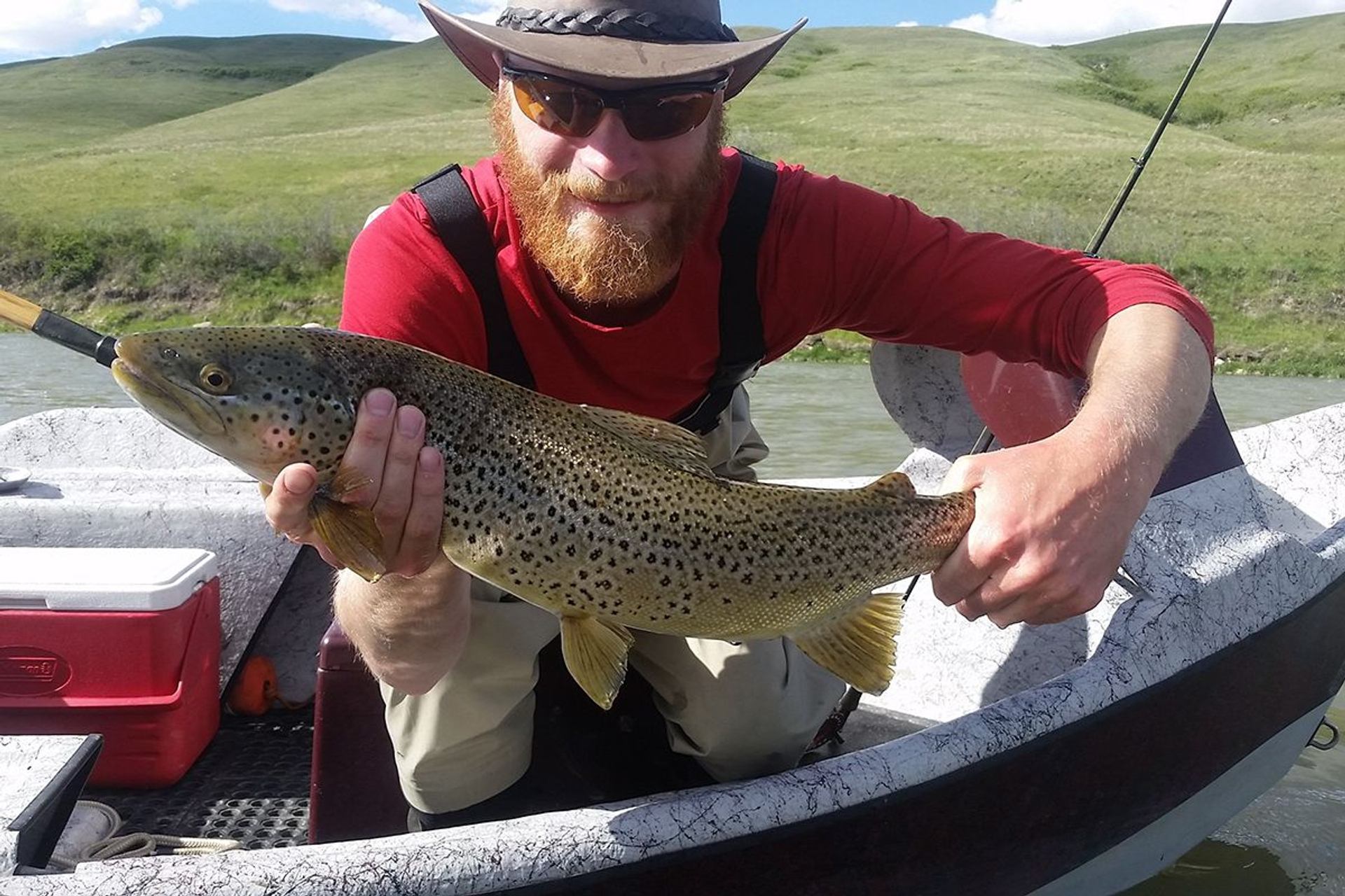 Bearded man in a red shirt holds a spotted fish.