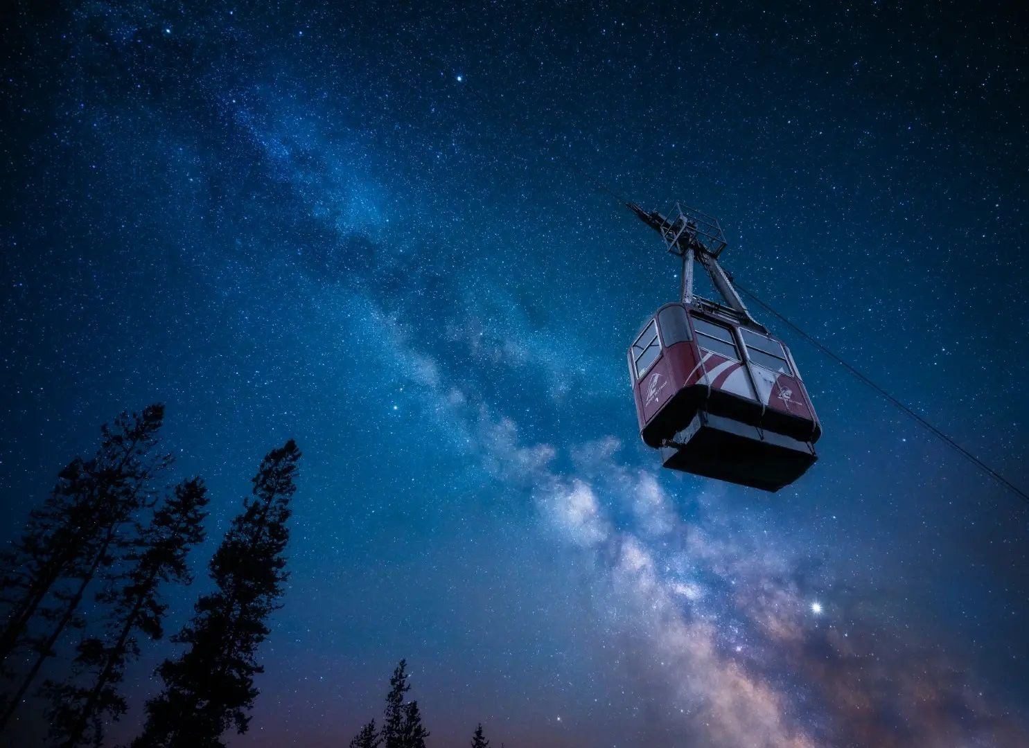 A gondola travel along a wire with a starlit sky above.