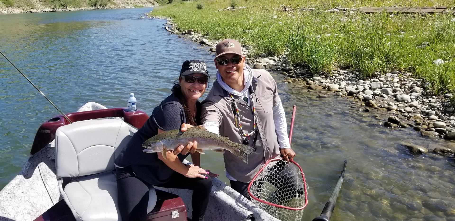 A woman and man hold a fish near the bank of a river.
