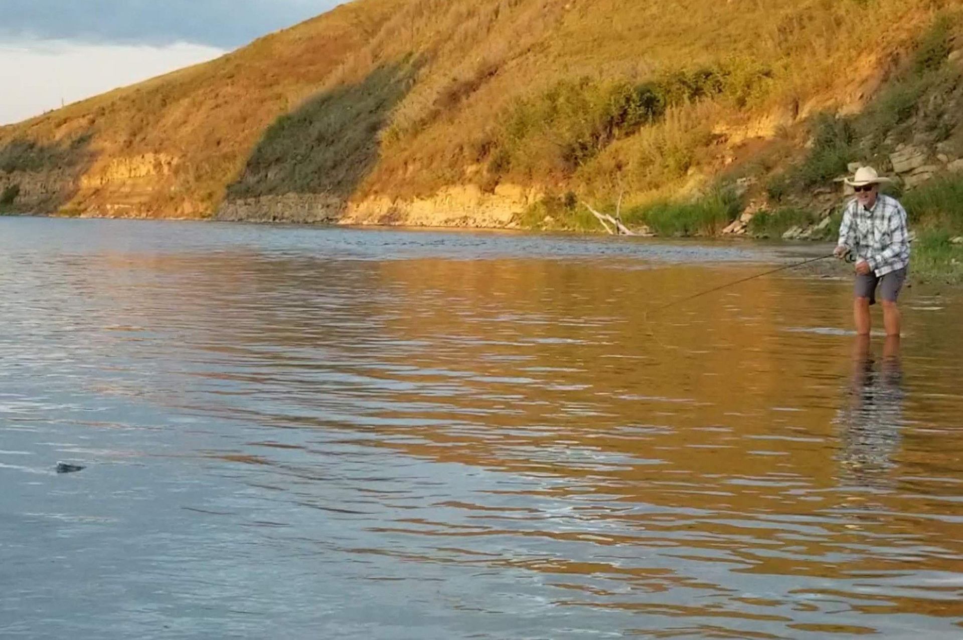 A man in a cowboy hat fly fishes in a river.