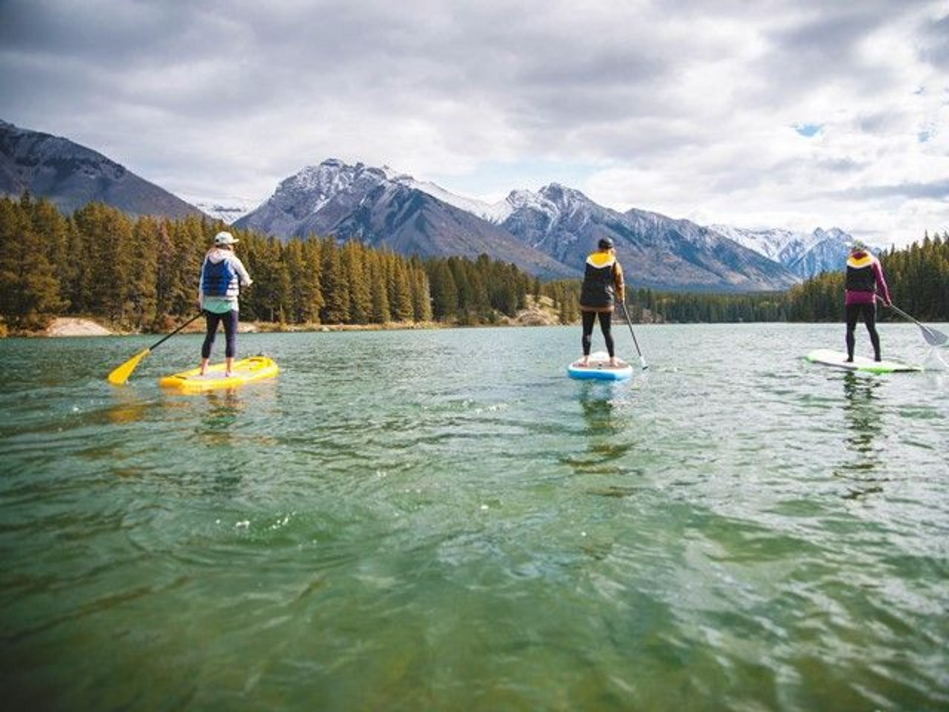 A group of three people stand up paddle boarding on Johnson Lake in Banff National Park.