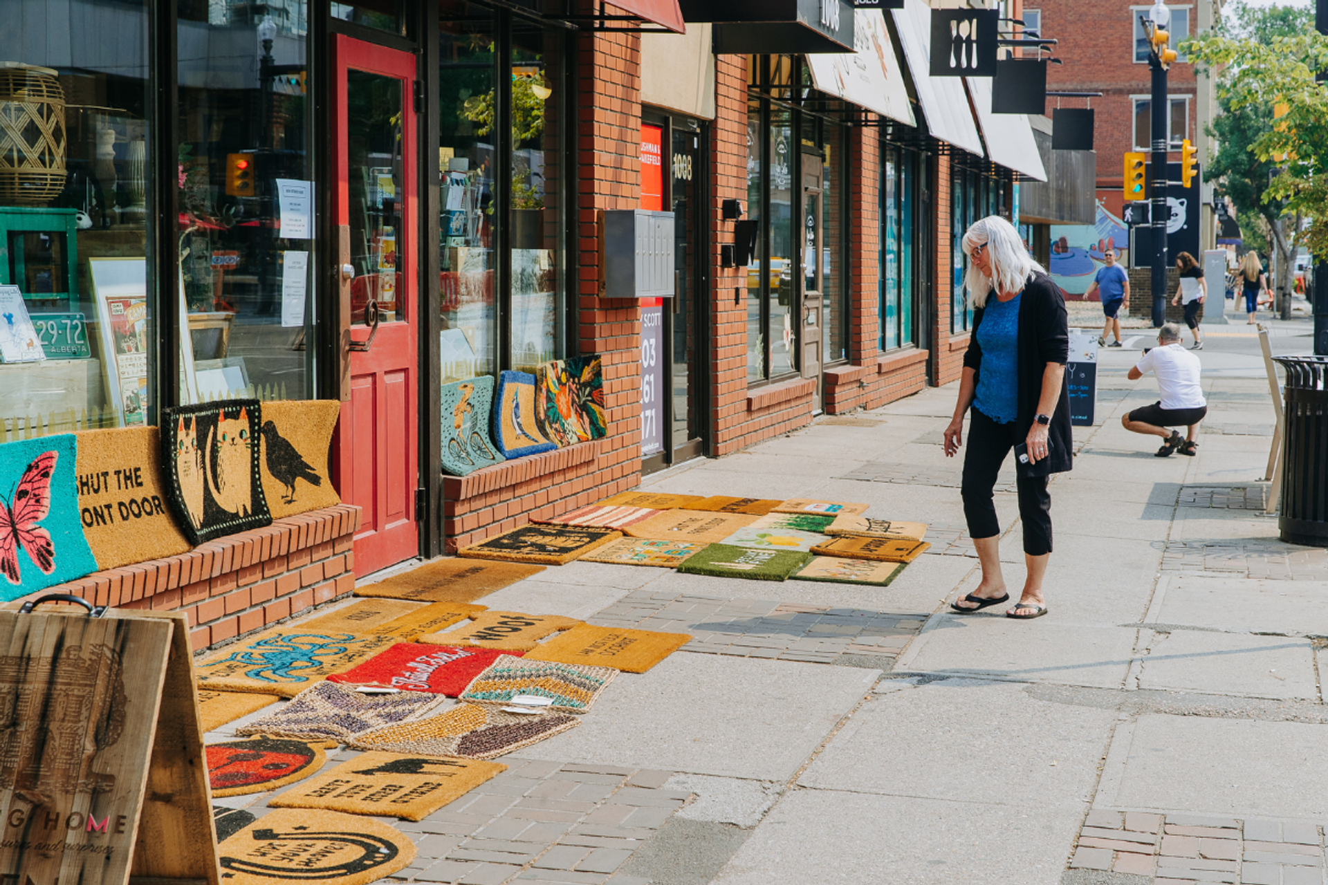 A woman looks at a range of welcome mats outside a shop.