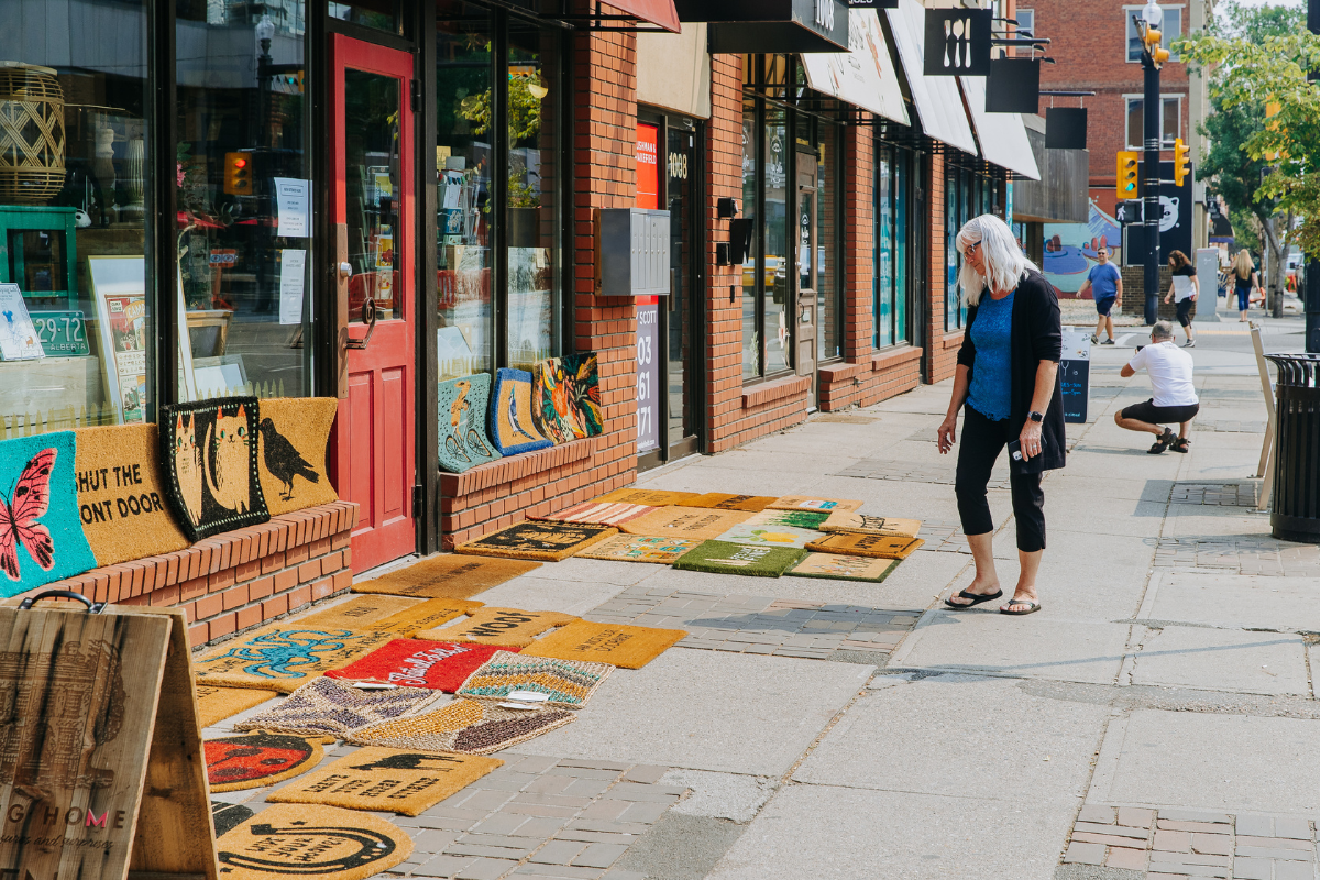 A woman looks at a range of welcome mats outside a shop.