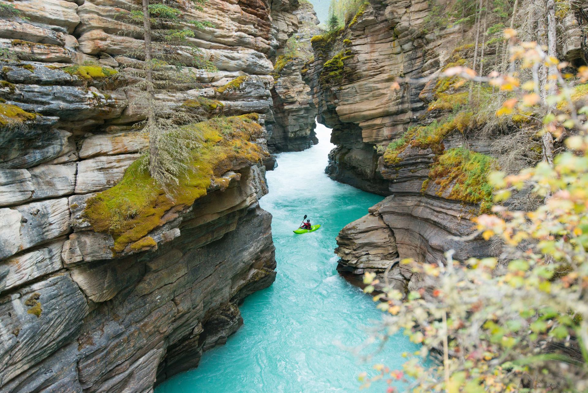 Scenic shot of kayaker paddling on a turquoise river through a narrow rock canyon at Athabasca Falls.