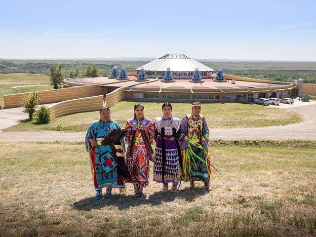 Siksika Blackfoot dancers standing in front of the Blackfoot Crossing Historical Park Interpretive Centre.