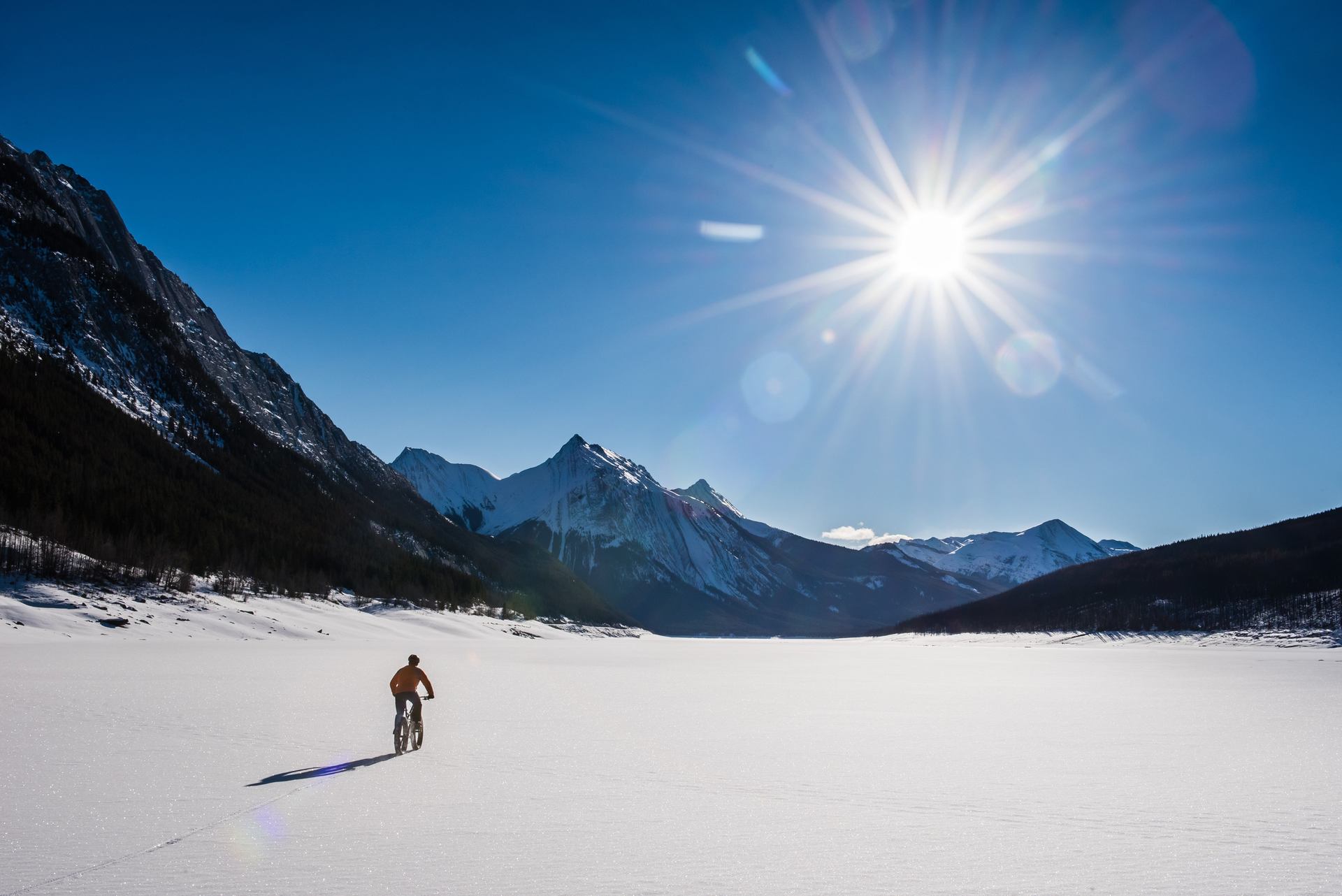 A man fat biking on Maligne Lake on sunny winter day in Jasper National Park.