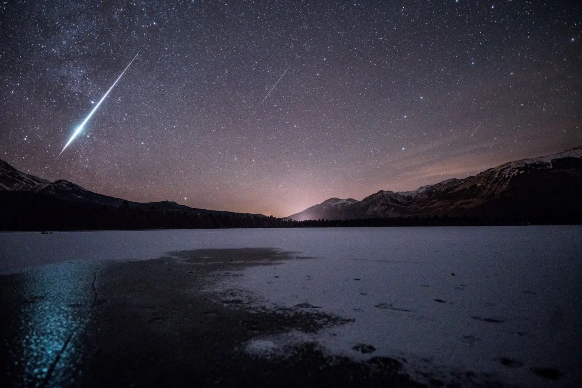 A starlit evening sky above a frozen lake and mountains peaks.