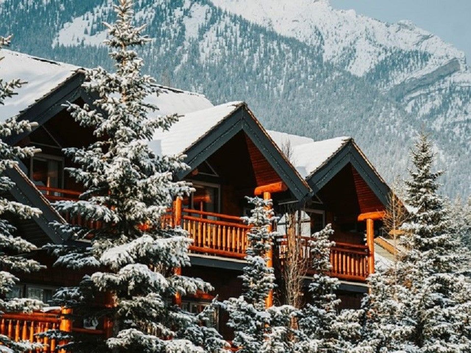 Snow covered log inn with snowy mountains in the background.