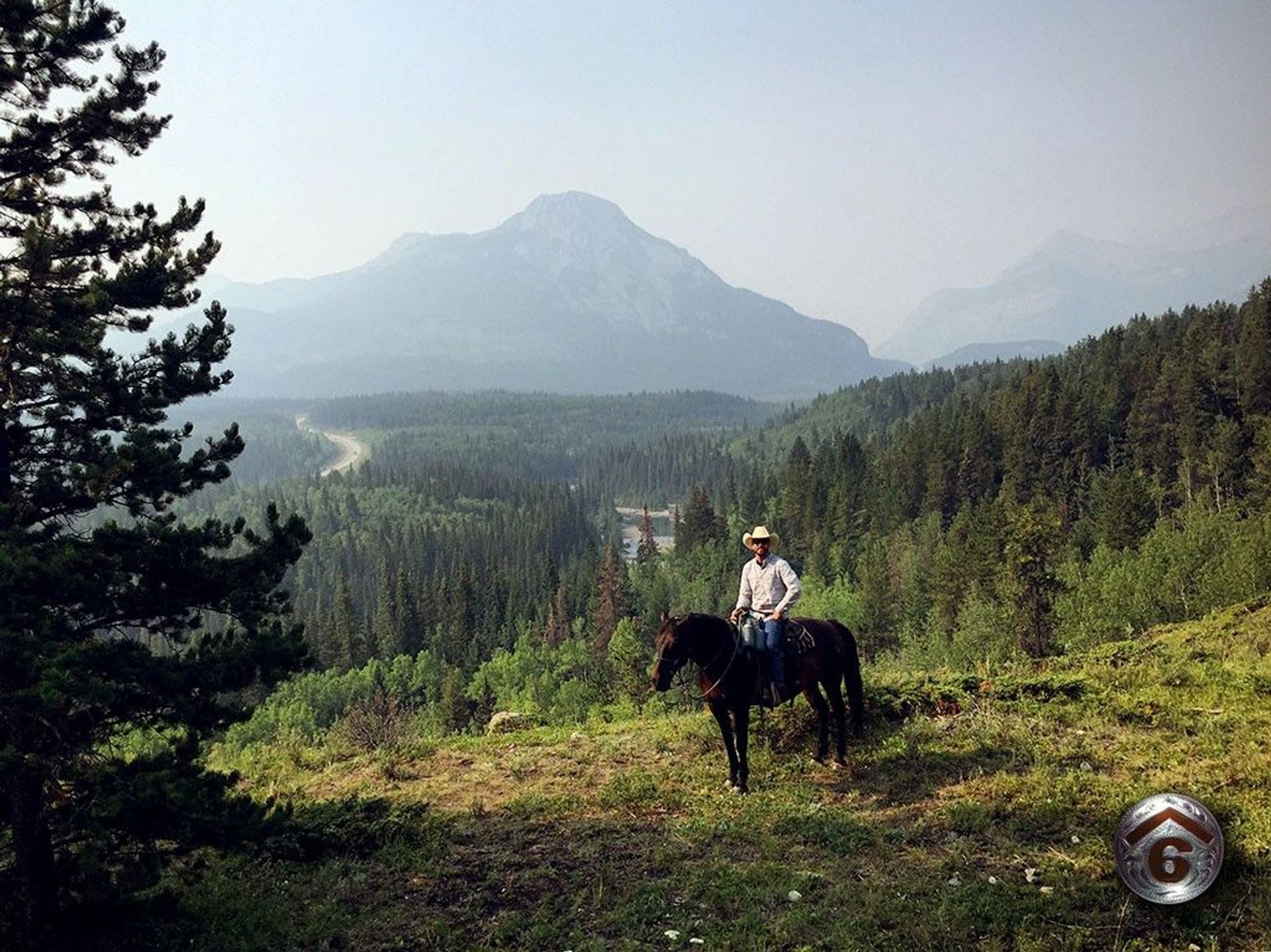 A rider on horseback poses in front of a misty mountain.