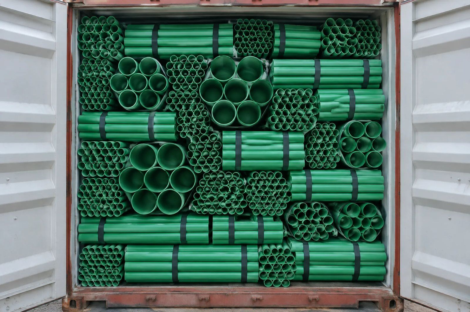 The open doors of a shipping container packed from floor to roof with strapped bundles of green PP-R pressure pipe in several diameters, the smaller bores nested into the gaps between the larger ones