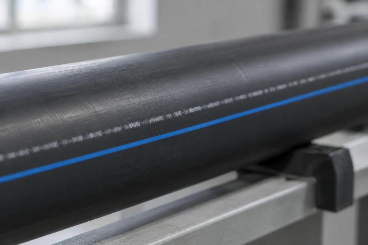 Close-up of a black HDPE pressure pipe with a blue identification stripe and a continuous white inkjet print line running along its length