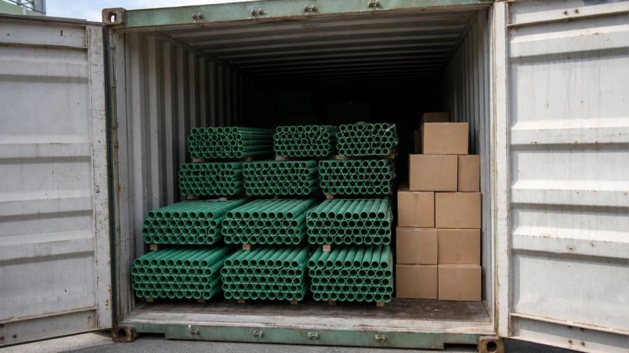 Open shipping container doors showing loose-stacked green PP-R pipe with open uncapped ends and cartons of fittings stacked to the right