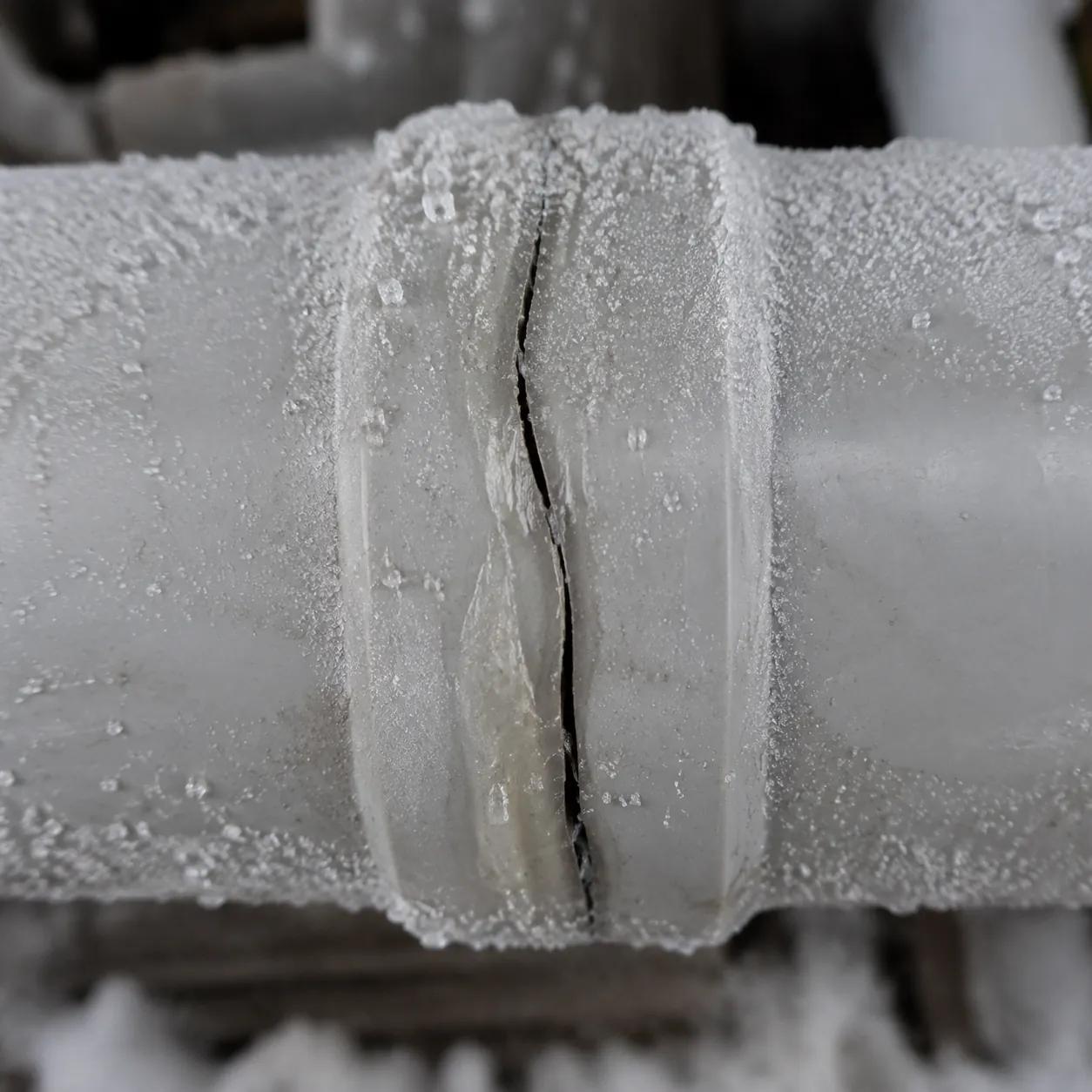Hyper-realistic macro photograph of a failed PPR fusion joint in freezing conditions, showing a longitudinal crack along the weld line, frost on the pipe exterior, metallic grey and white tones, industrial lighting, extreme detail, no text, no brand logo