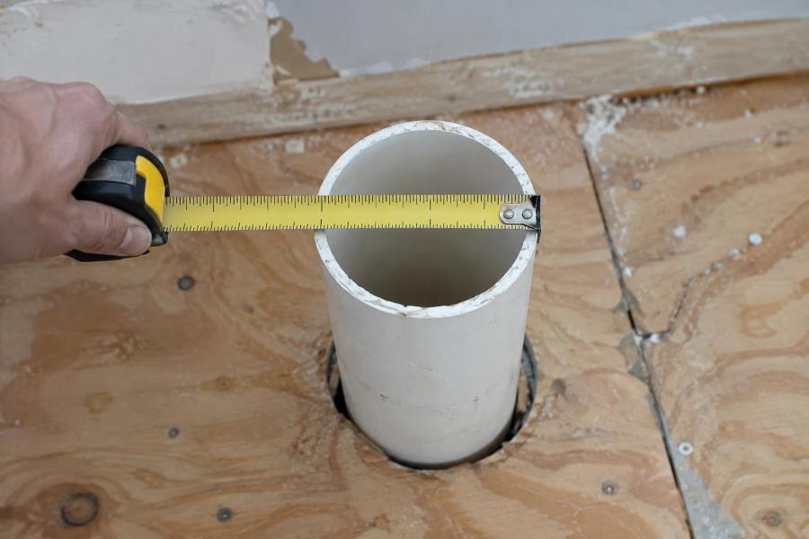 Measuring PVC drain pipe outside diameter with a tape to choose a toilet flange size