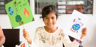 A young visitor to QAGOMA's Children's Art Centre holds up her climate placard and protest t-shirt designs / Photograph: Chloë Callistemon, QAGOMA