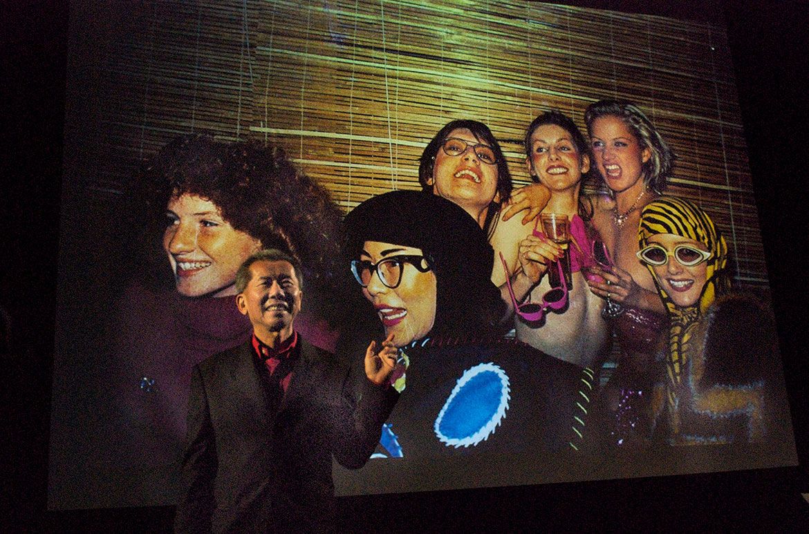 William Yang performing in front of an image from 1976 of Cressida Campbell, Jenny Kee and Stephen MacLean as part of his My Generation performance at the national Portrait Gallery, Canberra, December 2008 / Courtesy: William Yang