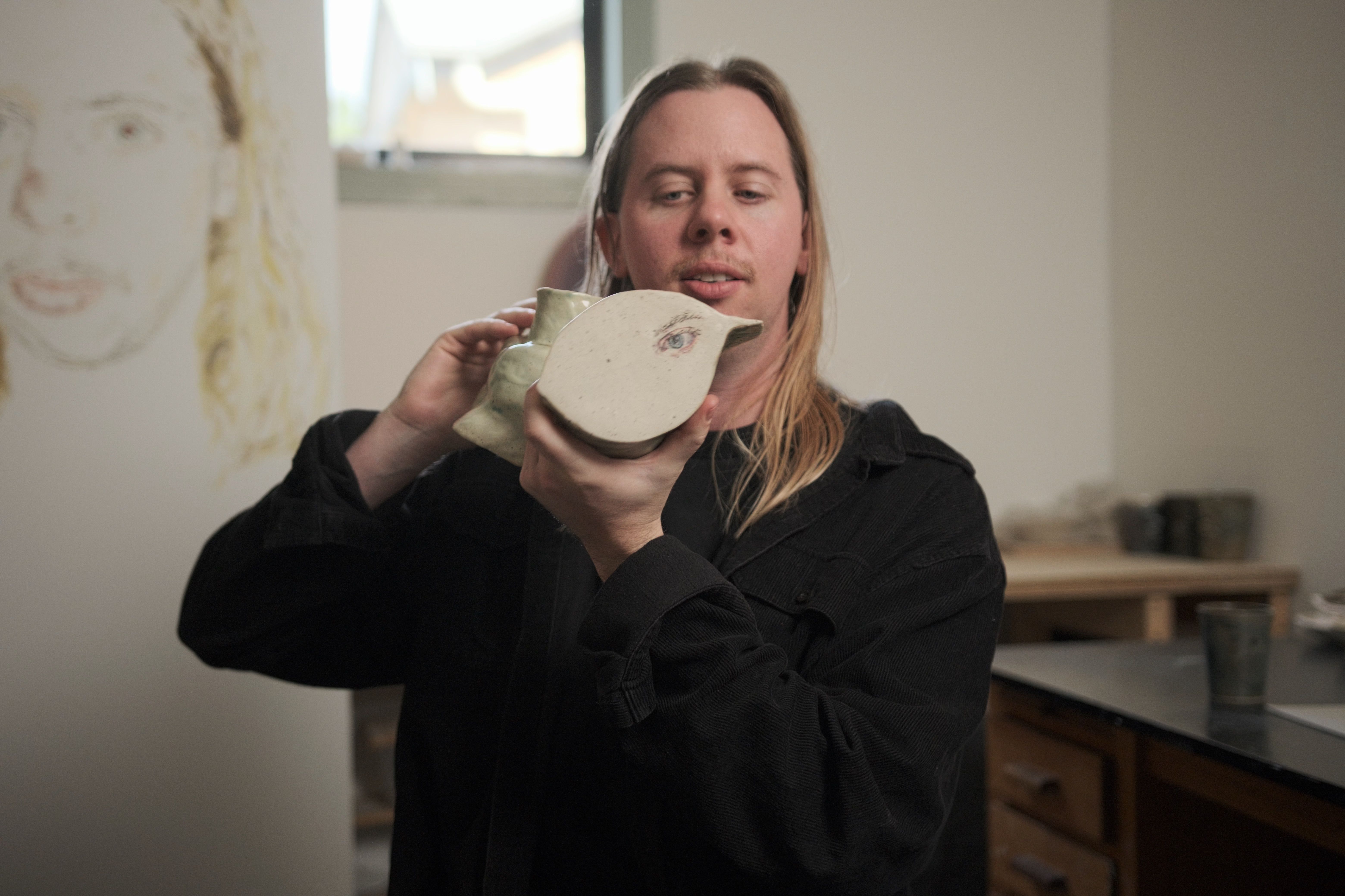 Artist Tyza Hart holding one of their ceramic sculptures, 2026 / Video still: J Virag © QAGOMA