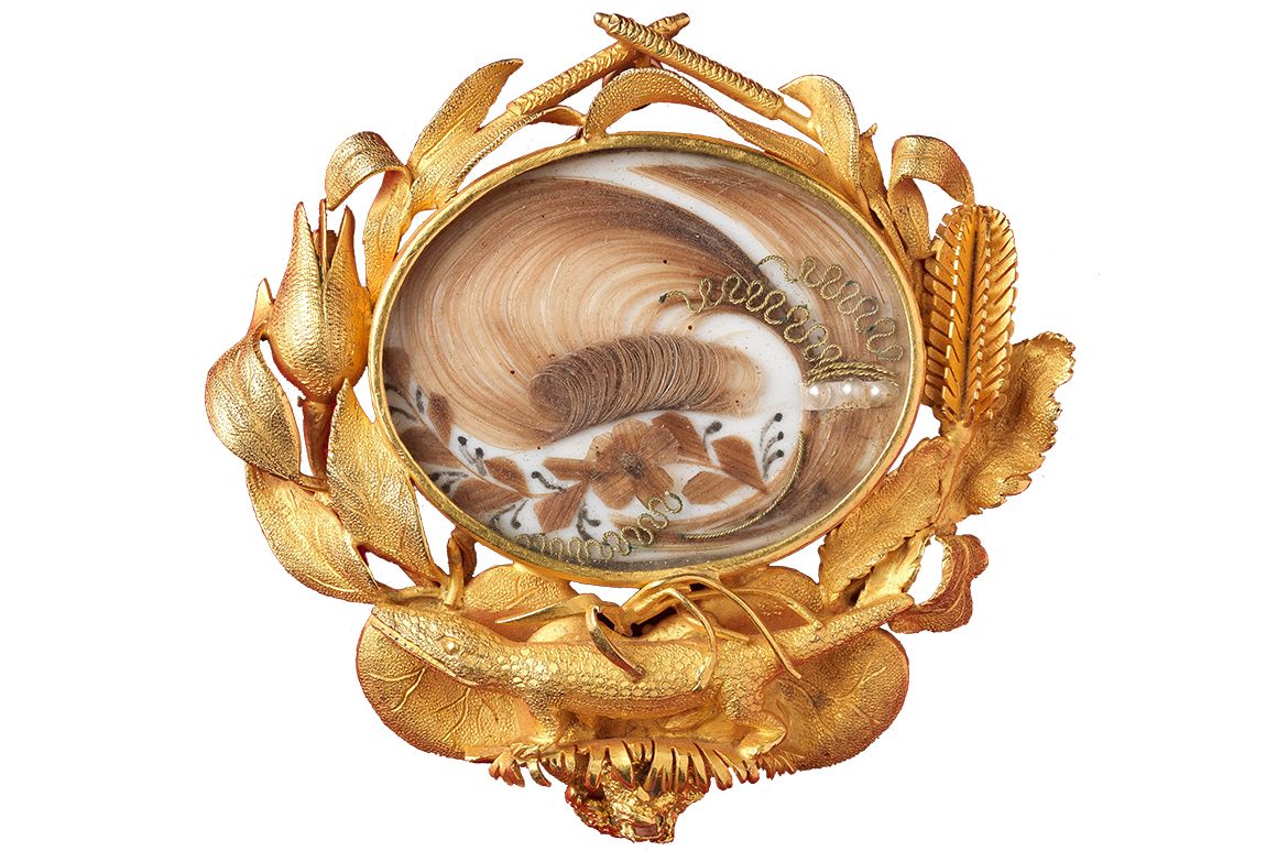 Hogarth, Erichsen & Co. (Manufacturer), Australia c.1854–65 / Julius Hogarth (Designer), Australia 1821–79 / Conrad Erichsen (Maker), Australia c.1825–1903 / Archer mourning brooch c.1860 / Matt gold with oval section (containing hair), embroidered over silk with seed pearls, chain and pin / 5.8 x 5.6 x 1.3cm / Gift of Mrs Alison Forster 1990 / Collection: Queensland Art Gallery | Gallery of Modern Art