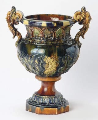 J L (James Laurence) Watts, Australia 1849–1925 / James Campbell & Sons, Australia 1885–1948 / Jardiniere c.1890 / Earthenware white clay body. The neck modelled with ivy leaves within arches, the swelling body with four sunflowers and leafy branches and the handles modelled as two grotesque masks. Glaze splashed clear brown, green and deep cobalt / 61 x 49 x 32.2cm / Gift of Miss Alison Campbell 1986 / Collection: Queensland Art Gallery | Gallery of Modern Art