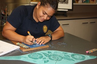 Nahkeeta Miller works on her lino while taking inspiration from Laurie Nona’s paddle design.