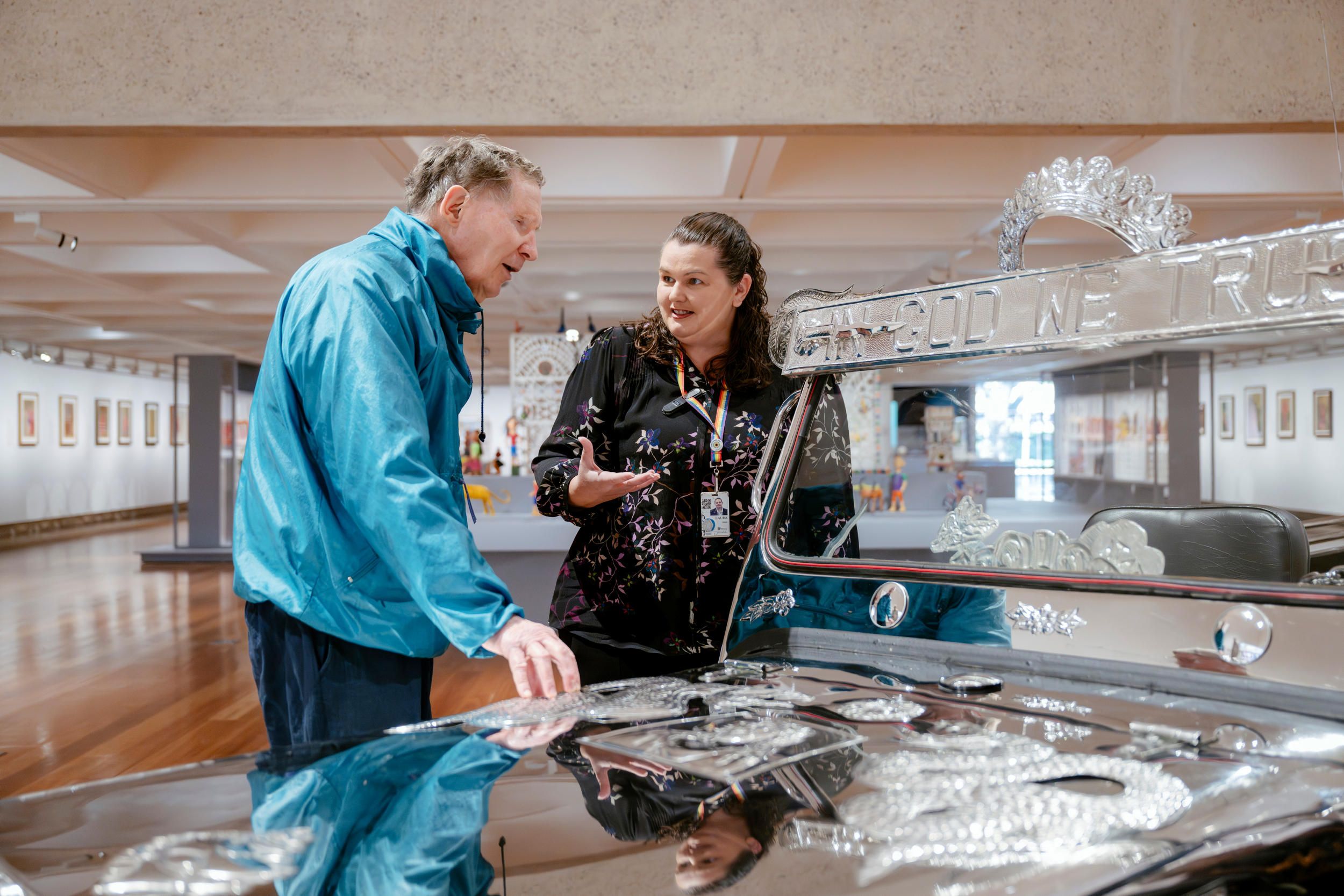 A staff member supporting a visitor who is blind to explore In God we Trust (version 2) 2009 by Isabel Aquilizan and Alfredo Aquilizan/ Stainless steel, rubber, vinyl, glass, painted board, Jeep parts / Gift of anonymous donors through the Queensland Art Gallery | Gallery of Modern Art Foundation 2025. Donated through the Australian Government’s Cultural Gifts Program / Collection: Queensland Art Gallery | Gallery of Modern Art / Photograph: Joe Ruckli