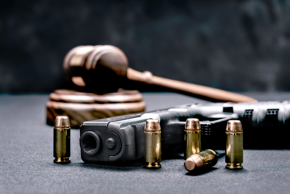 Image A wooden gavel, a handgun, and several brass bullets on a dark grey surface, symbolizing California firearm laws and legal defense.