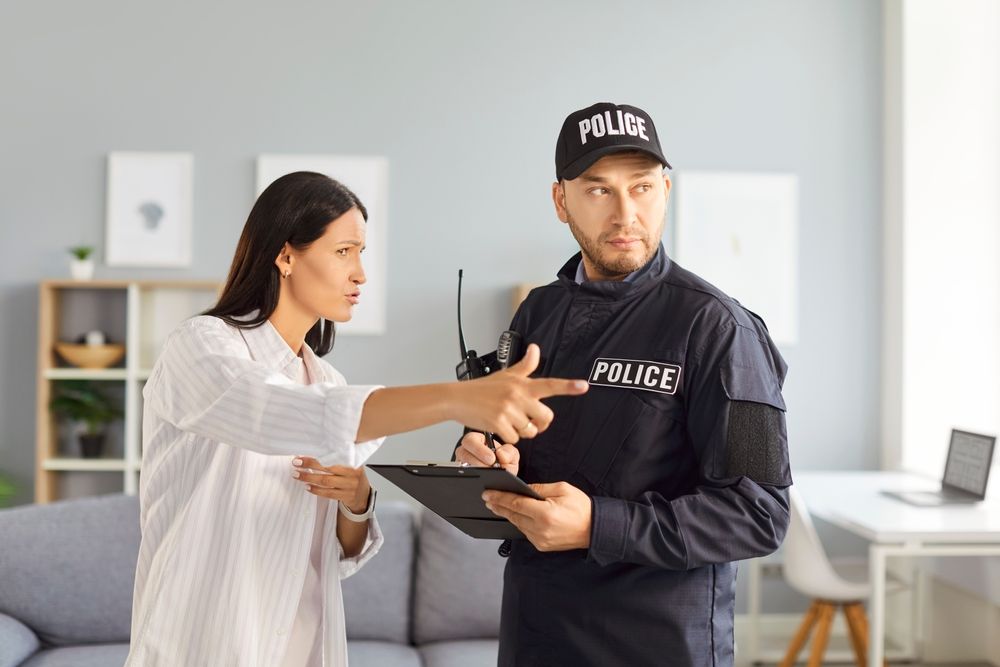 A woman reporting an incident to a police officer holding a clipboard, illustrating the common misconception of a victim "pressing charges" in California, a power held only by prosecutors.