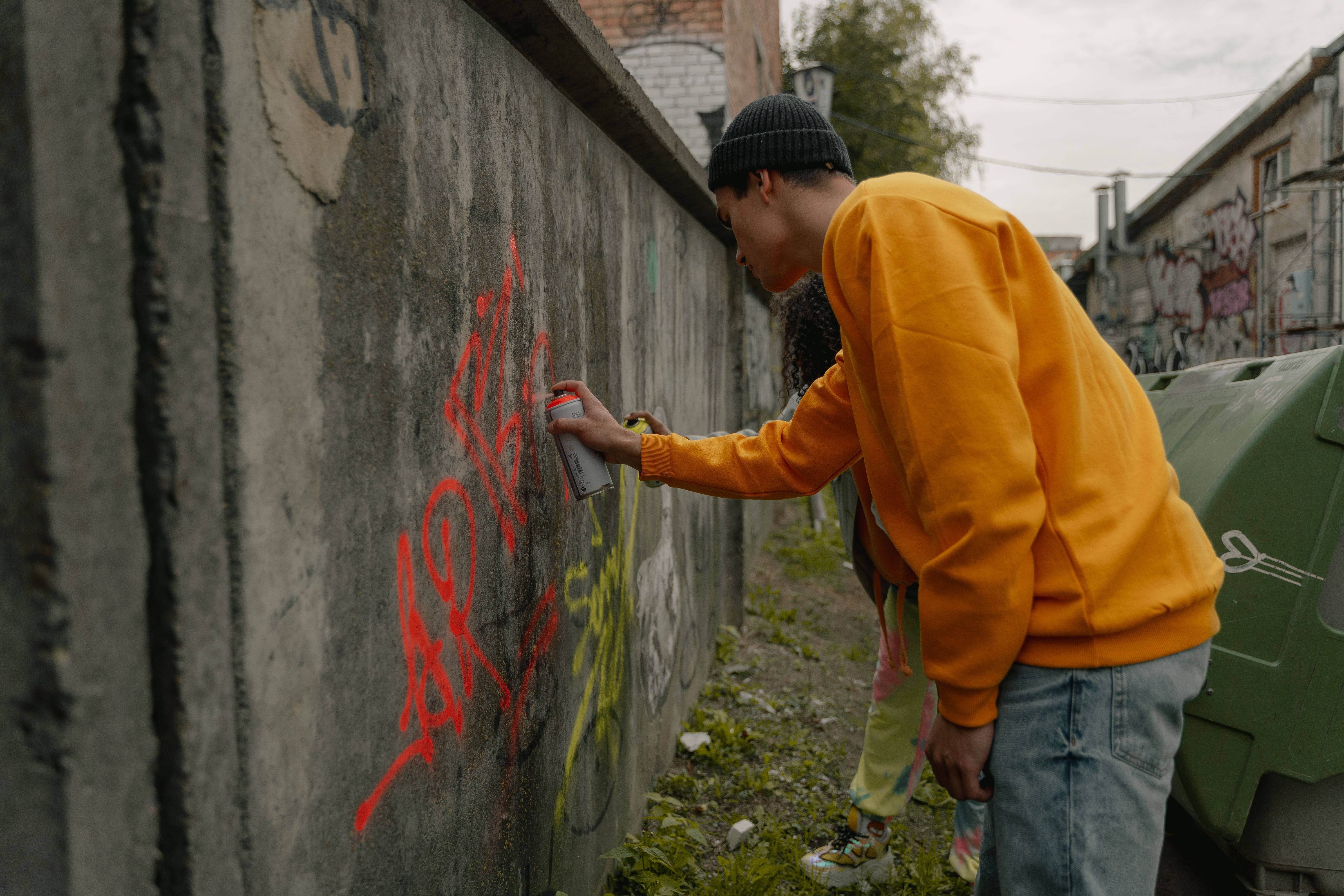 Image Teen in an orange hoodie spray-painting graffiti on a wall, an example of vandalism behind juvenile crime charges in Los Angeles
