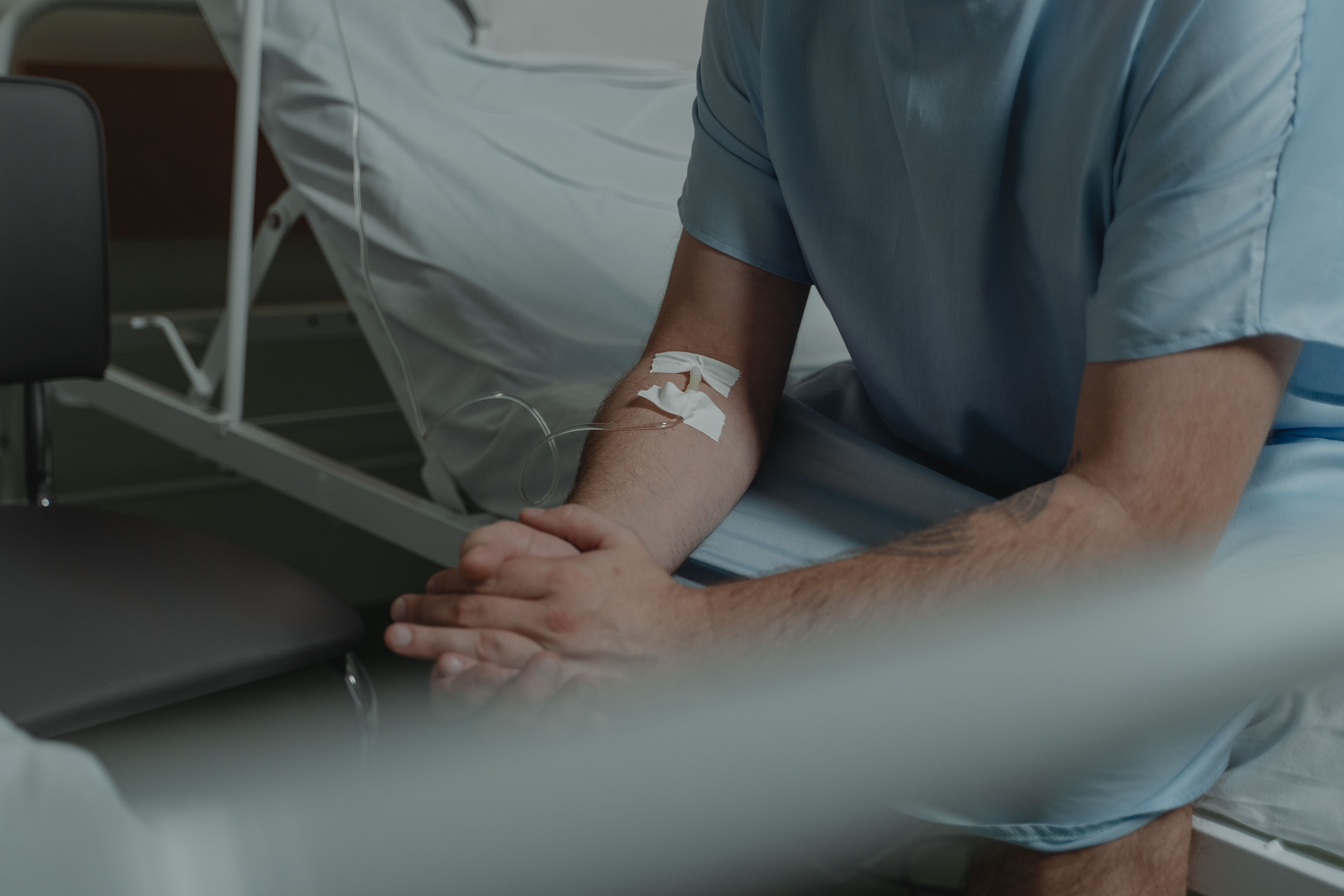 Patient in a hospital gown sitting on a bed with an IV taped to his arm, illustrating how a chronic illness can cause a missed court date in California.