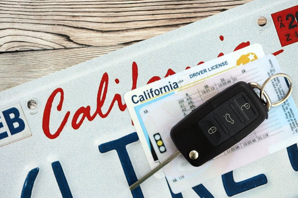 A California driver's license and modern car key fob resting on a California "CAL" license plate, representing the path to legal license restoration.