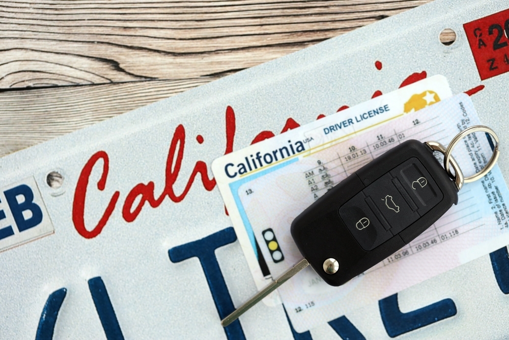 Image A California driver's license and modern car key fob resting on a California "CAL" license plate, representing the path to legal license restoration.