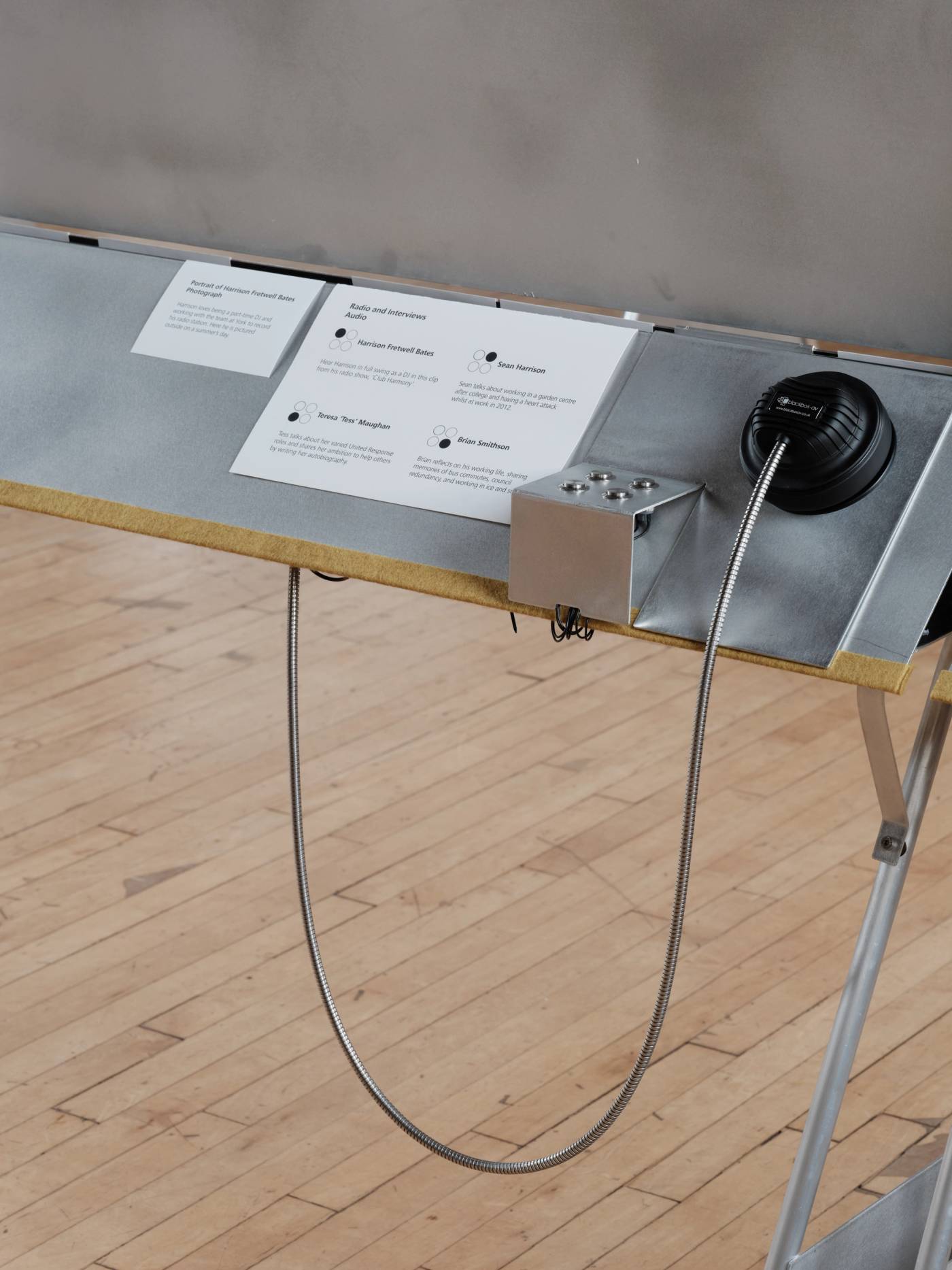 A detail of an aluminium showcase design with a ledge holding printed caption panels and a listening device