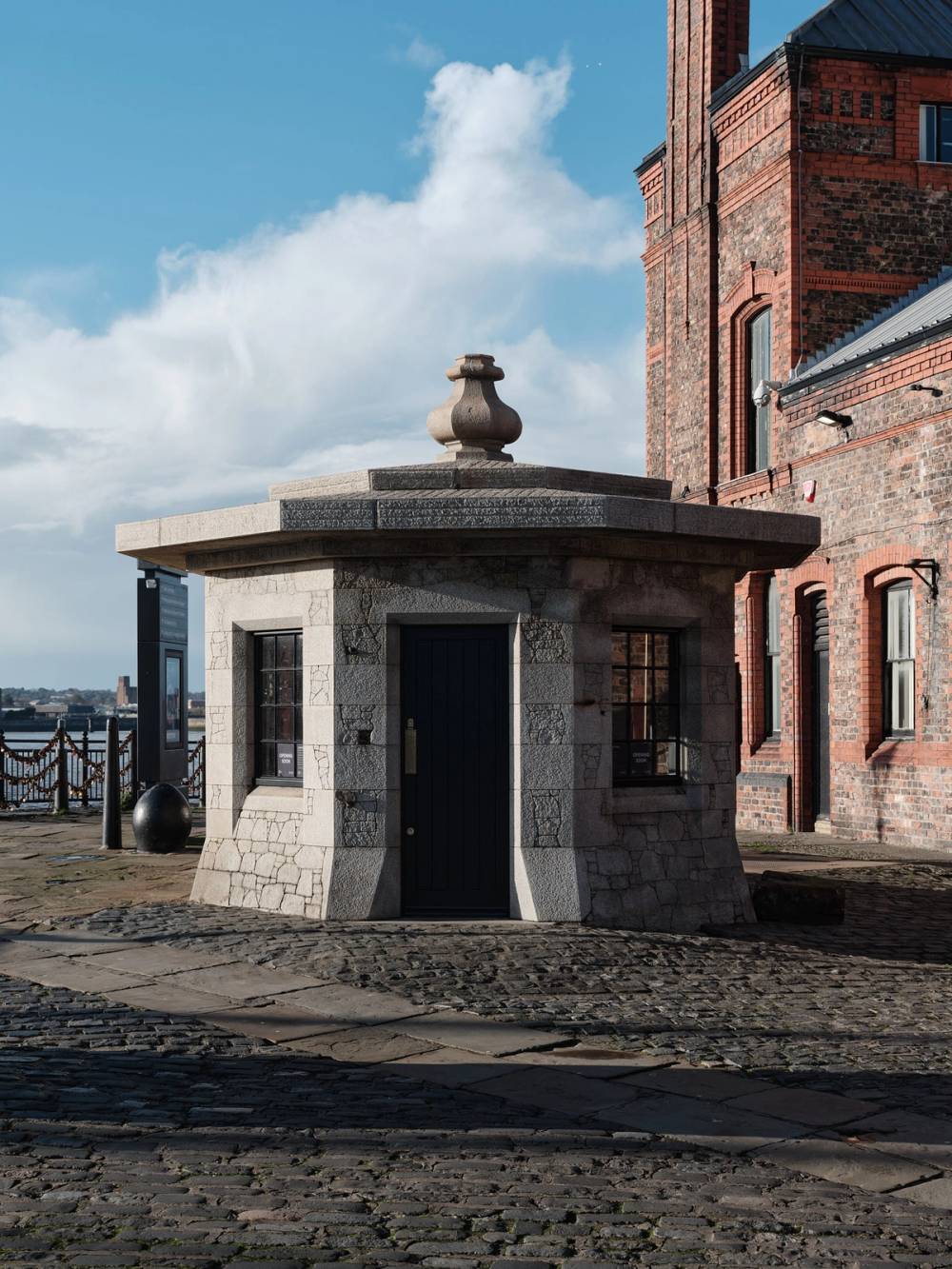 A photograph of a stone hut with open door on a waterfront
