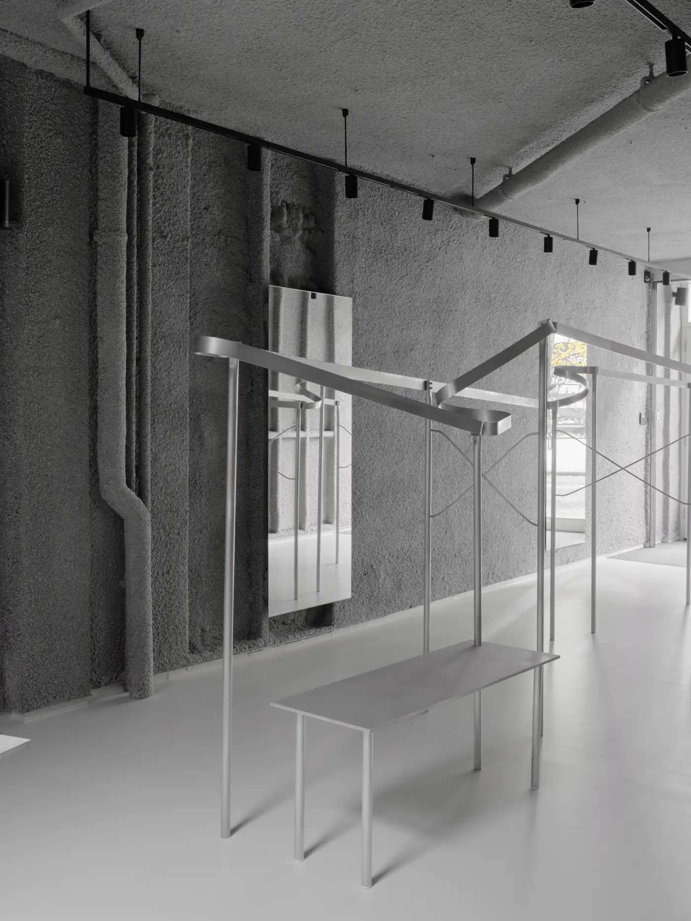 Menswear store interior featuring dark grey, highly textured sprayed paper pulp walls and ceiling, contrasting with sleek, light grey bespoke aluminium display rails and a matching rectangular table.