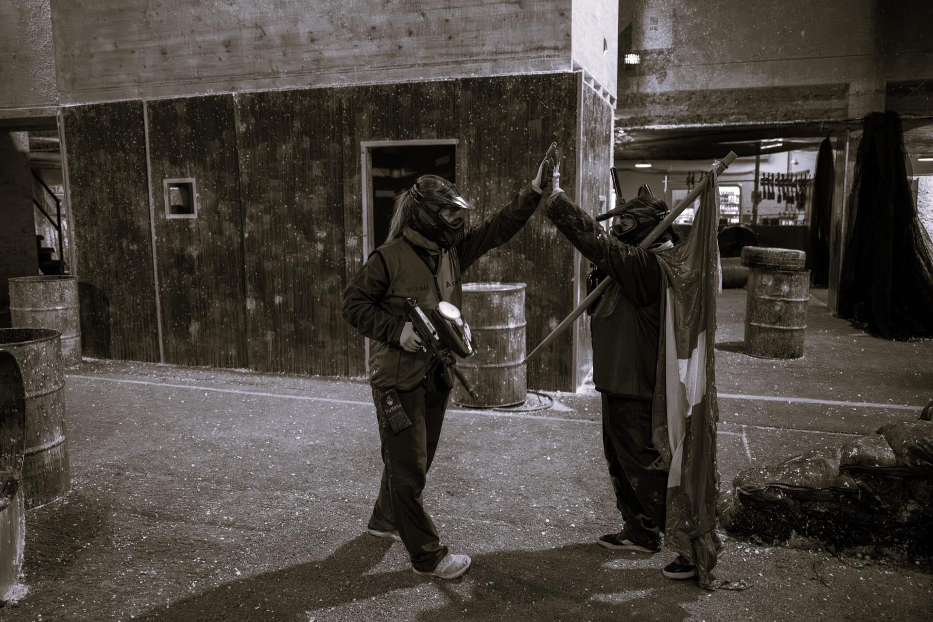 Zwei Paintball-Spielende klatschen sich in der Halle ab, eine Person hält eine Fahne