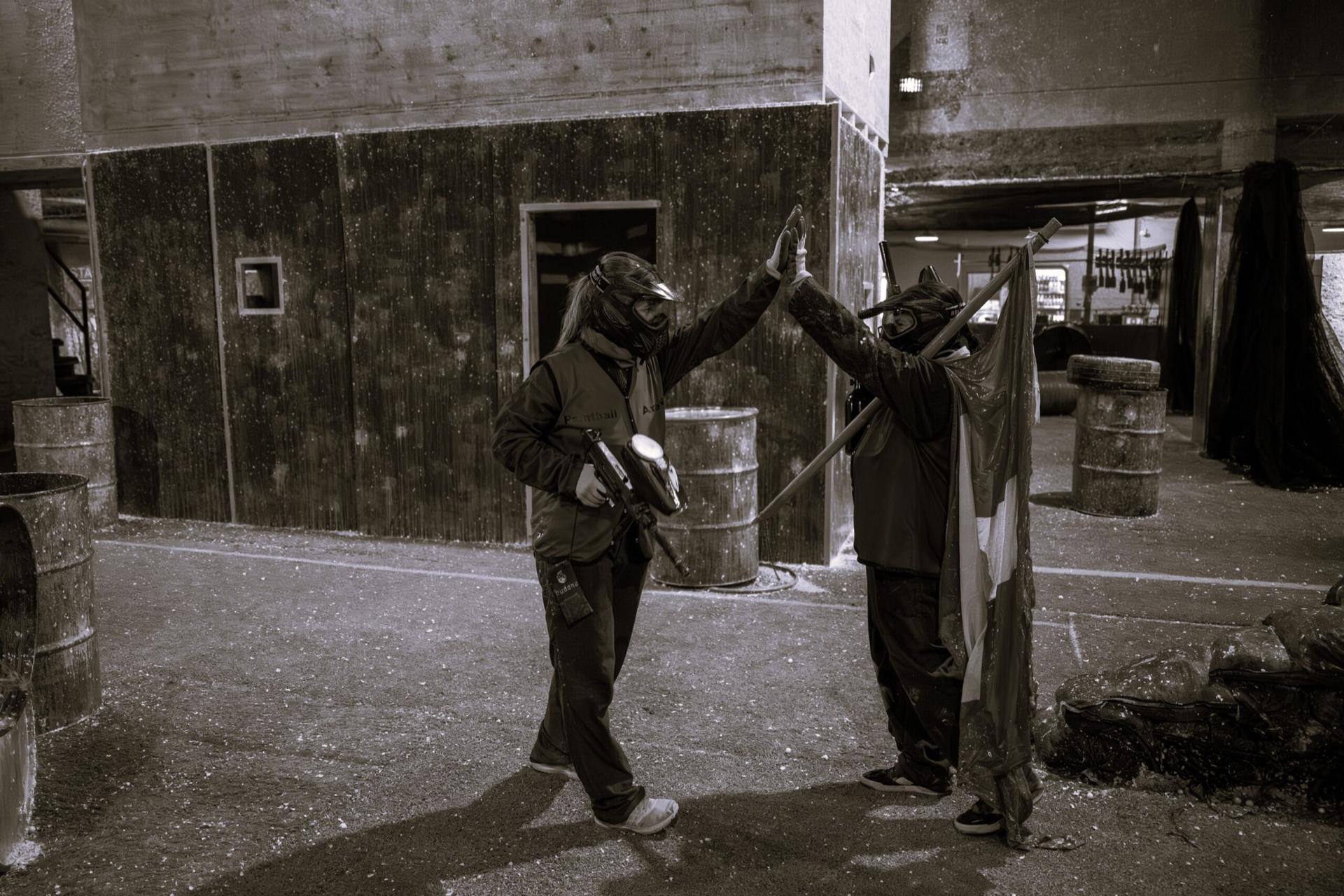 Zwei Paintball-Spielende klatschen sich in der Halle ab, eine Person hält eine Fahne