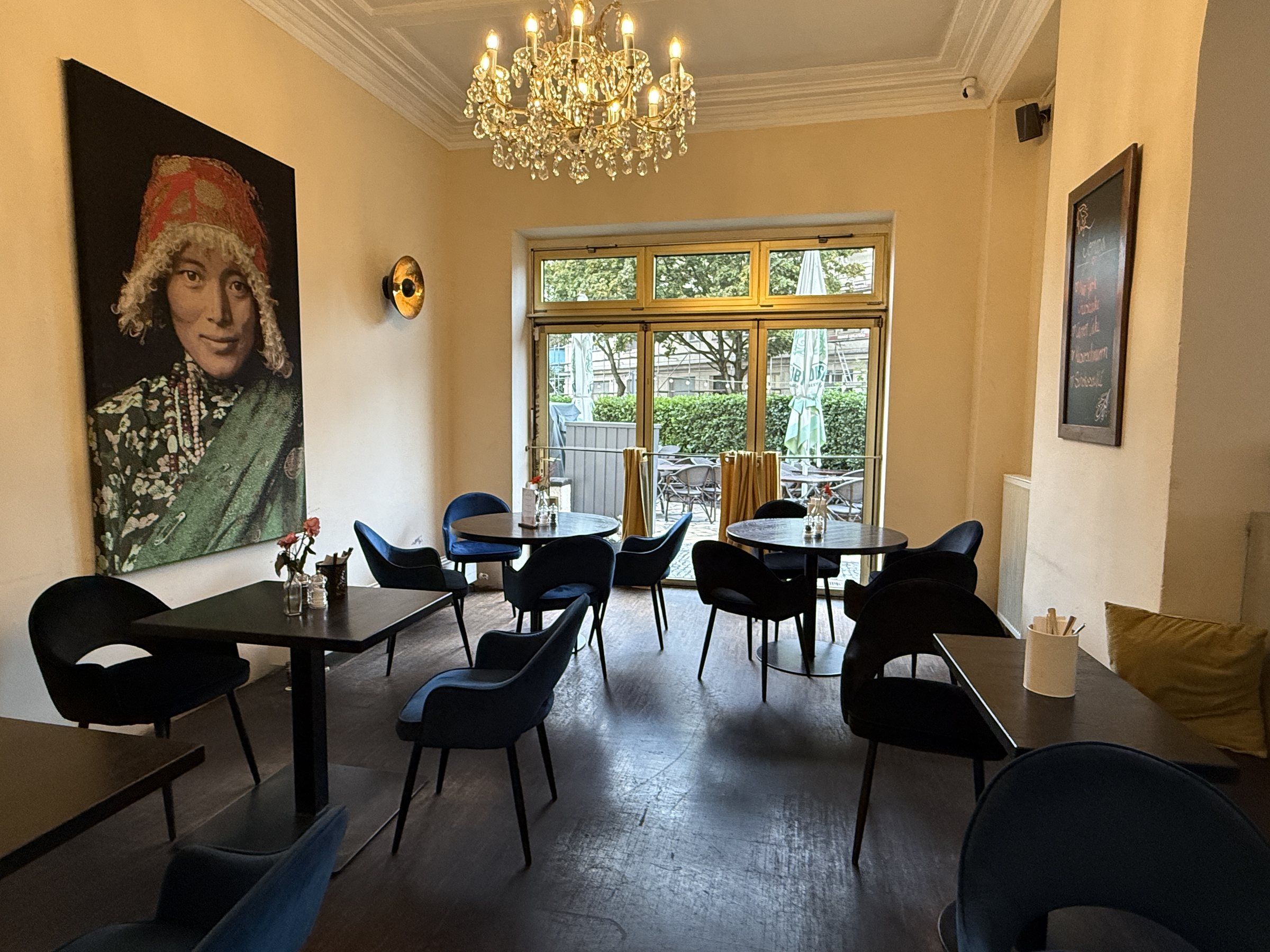 Das kleine Zimmer mit Kronleuchter, großem Porträt an der Wand und Fenstertür zur Terrasse