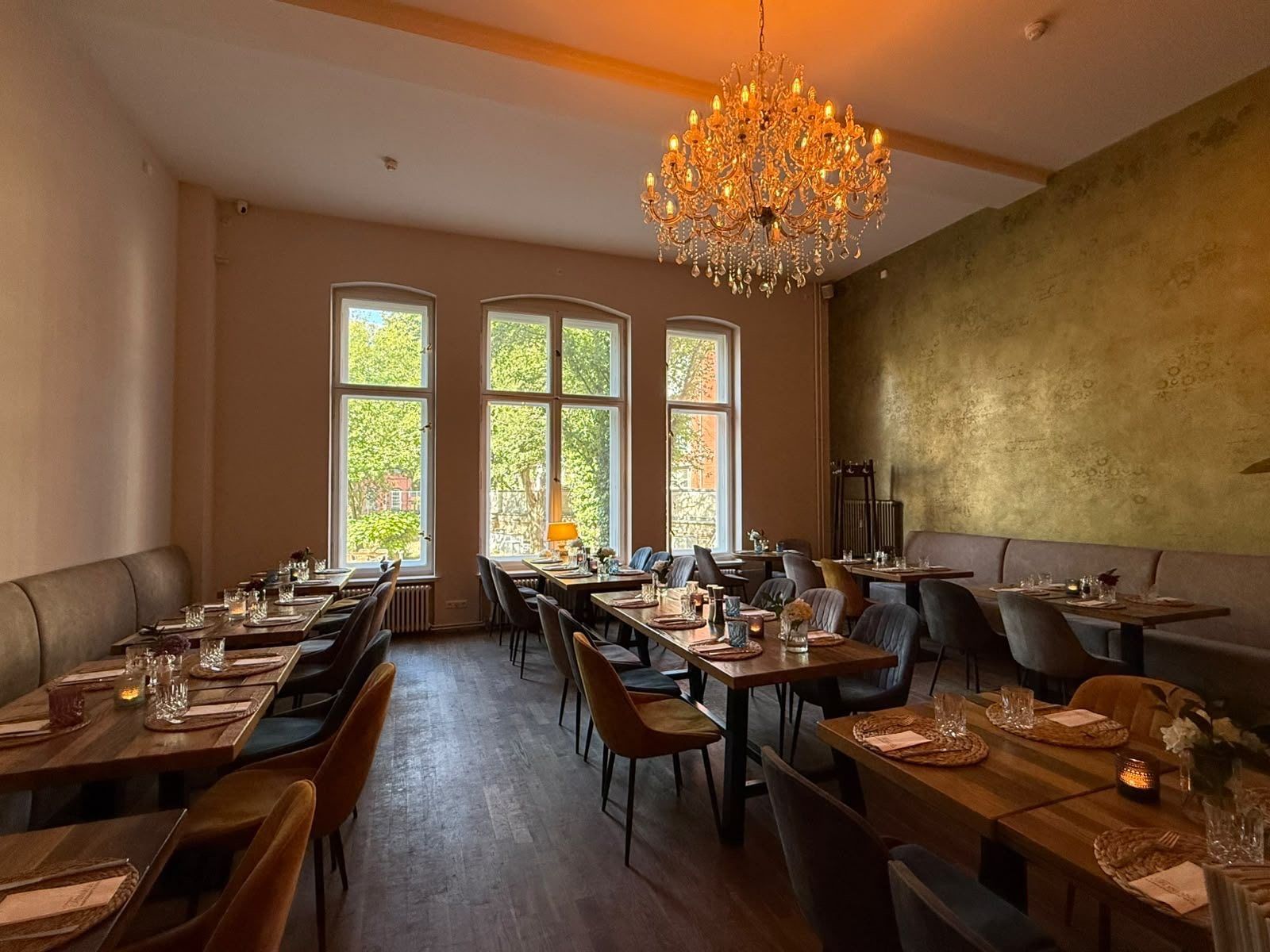 Der hintere Bereich mit hohen Bogenfenstern, goldener Wand, Kronleuchter und gedeckten Tischen