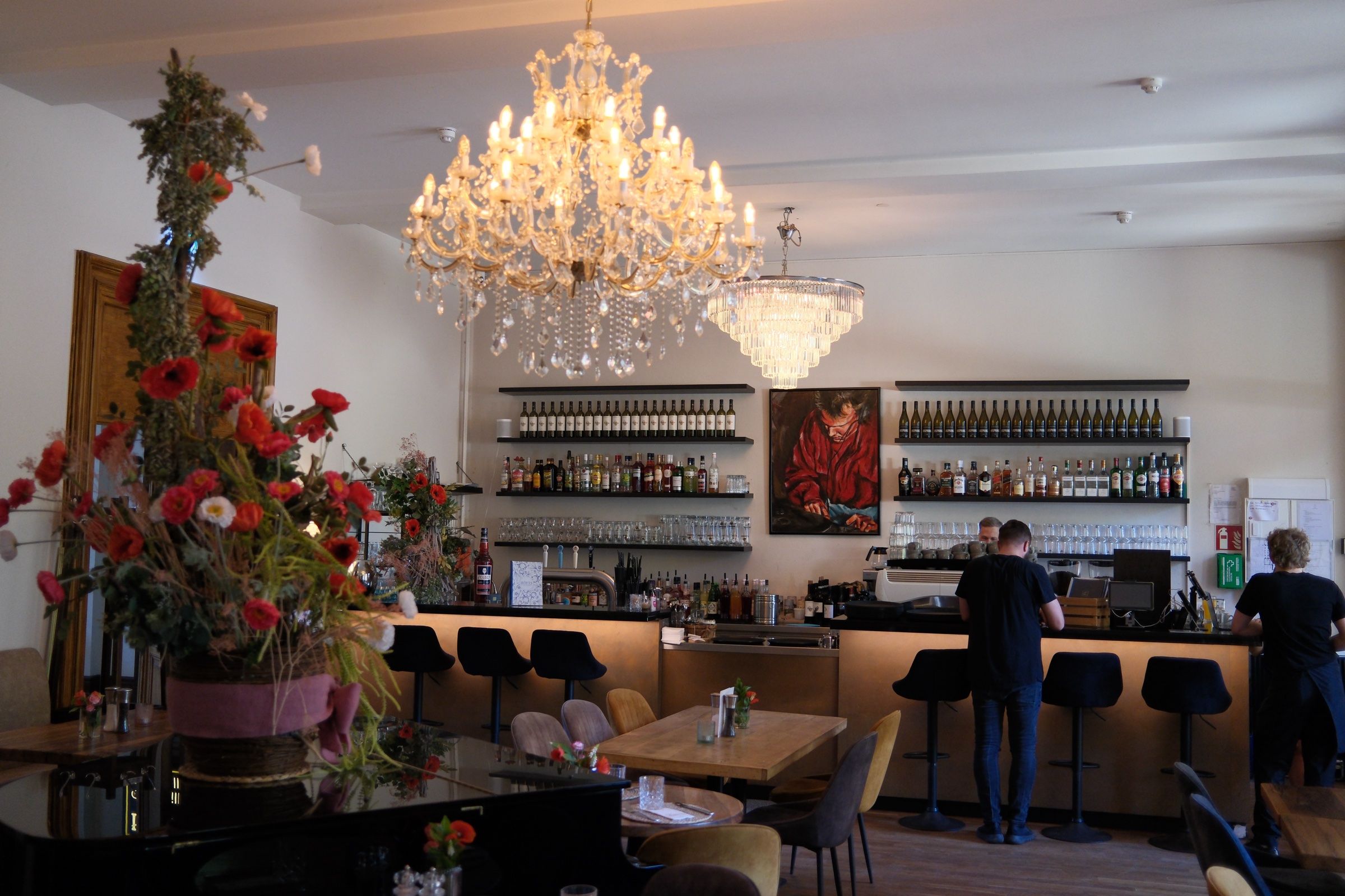 Bar des TOMASA Potsdam unter dem Kronleuchter, davor ein großes Blumenarrangement